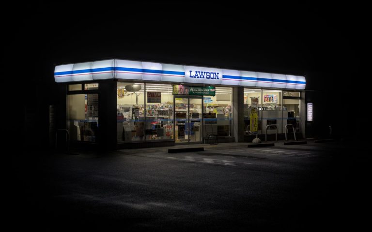 Exterior view of a Lawson convenience store at night in Japan, highlighting urban life.