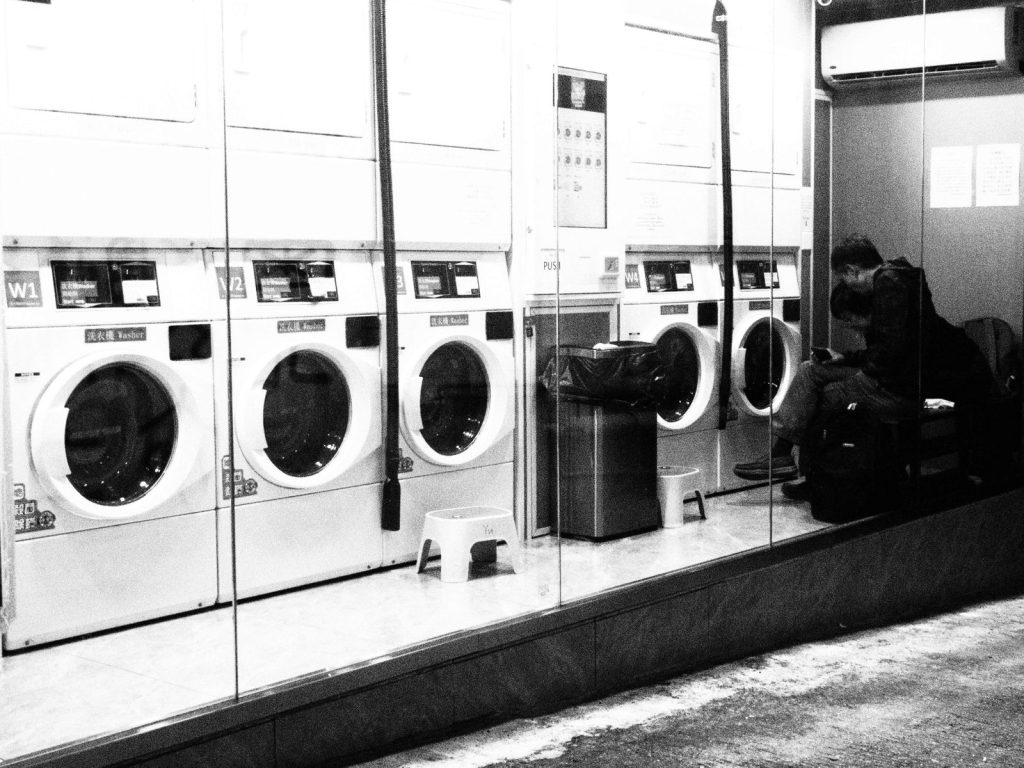 A black and white photo capturing a quiet moment inside a Hong Kong laundromat at night.