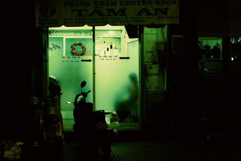 A dimly lit clinic entrance at night with motorbikes parked outside, casting a mysterious vibe.