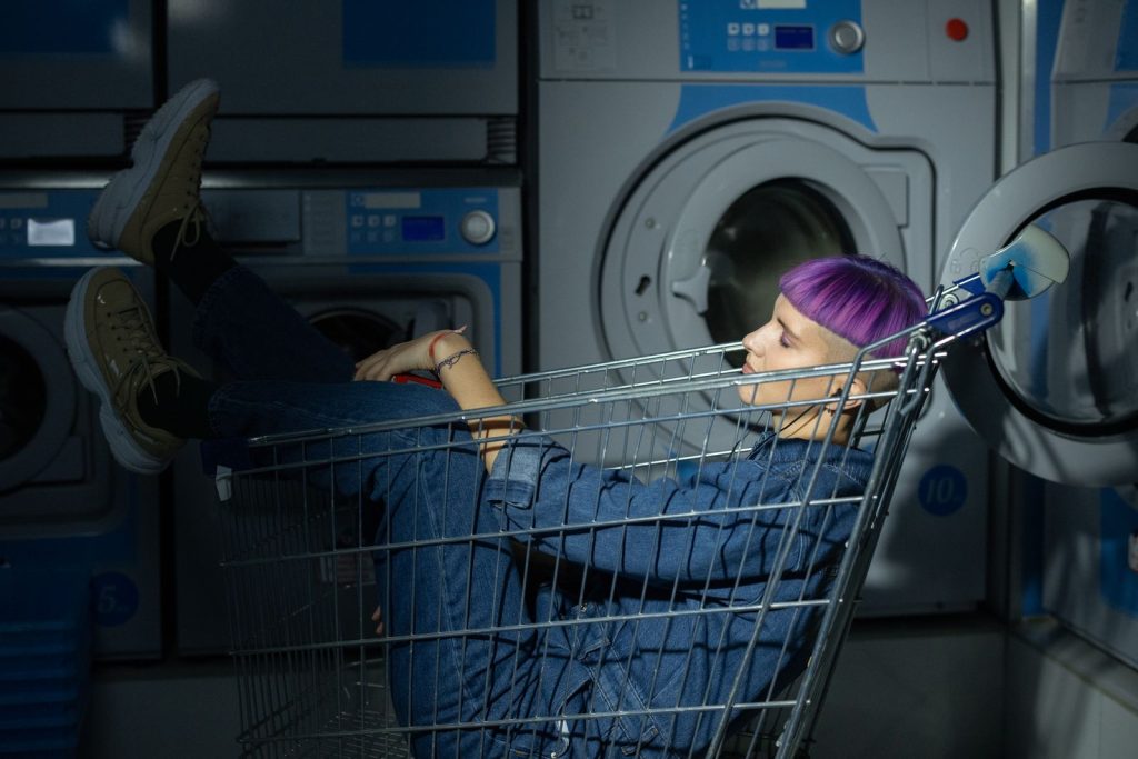 A unique portrait featuring a person with dyed hair lounging in a shopping cart inside a laundromat.