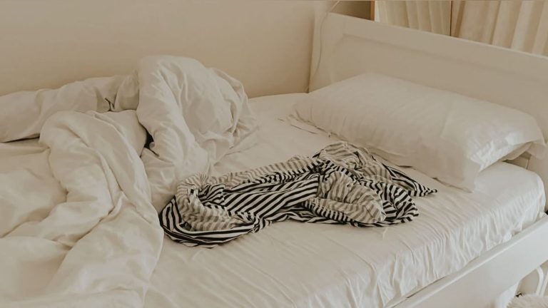 An unmade bed with crumpled linens and a striped shirt adding a cozy feel.