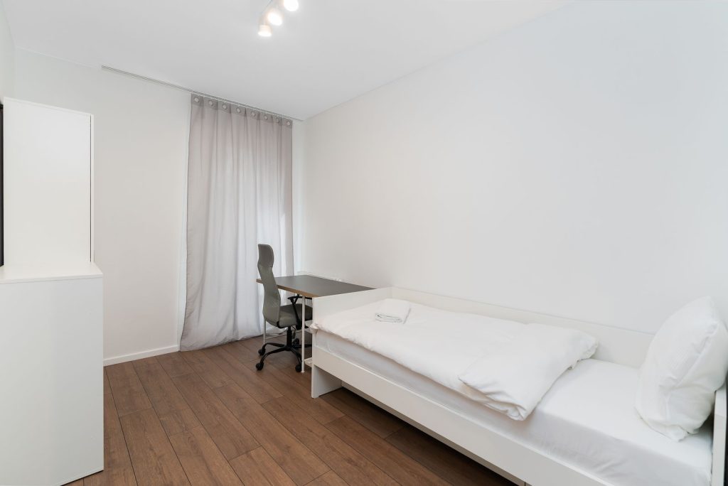 Bright minimalist bedroom with a single bed and desk, ideal for modern living.