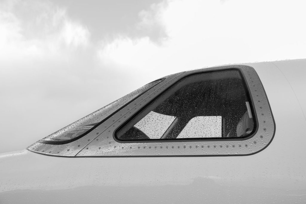 Close-up of rain-speckled airplane window in grayscale, showcasing aviation detail.