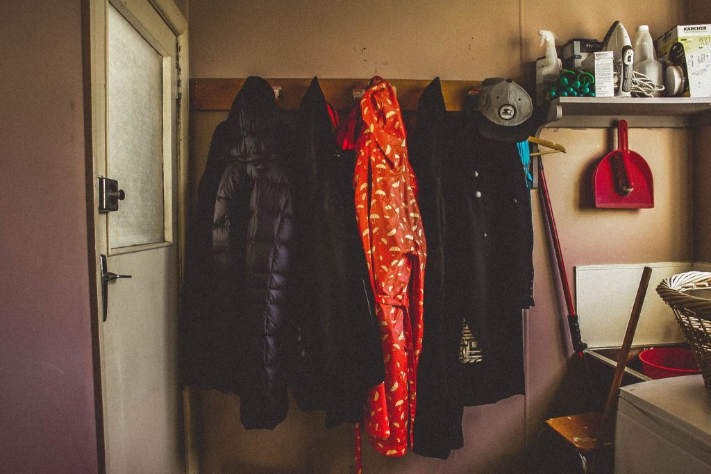 A vibrant rain jacket is hanging with black coats in a cozy laundry room.