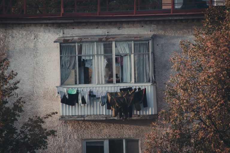 Clothes drying on a balcony of an old urban building with trees nearby.