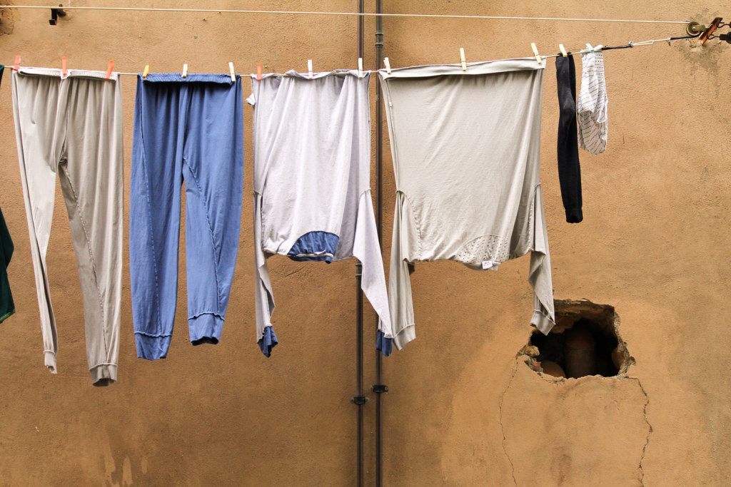 A variety of casual clothes hanging fresh on an outdoor clothesline against a weathered wall.