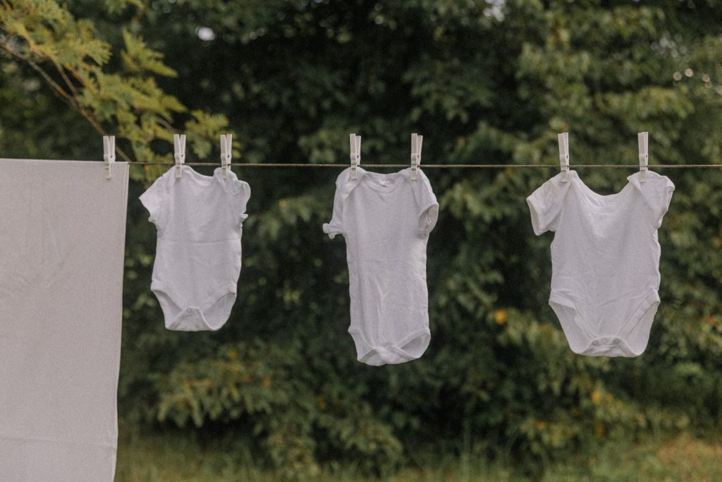 White baby onesies hanging on a clothesline outside, drying in the fresh air.