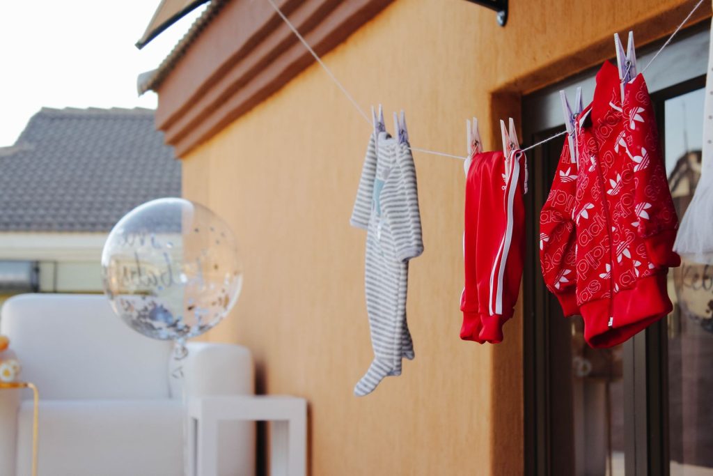 Baby clothes hanging on a clothesline next to a clear balloon against a wall.