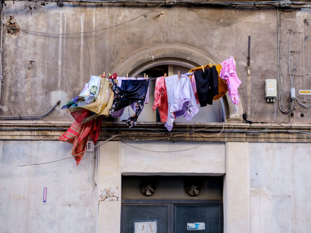 Vibrant clothes hanging on a clothesline against a rustic Sicilian building facade in Catania.
