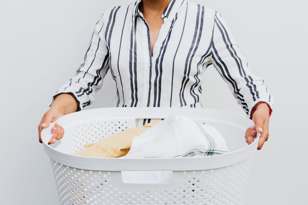 A woman holding a laundry basket filled with clothes against a plain white background.