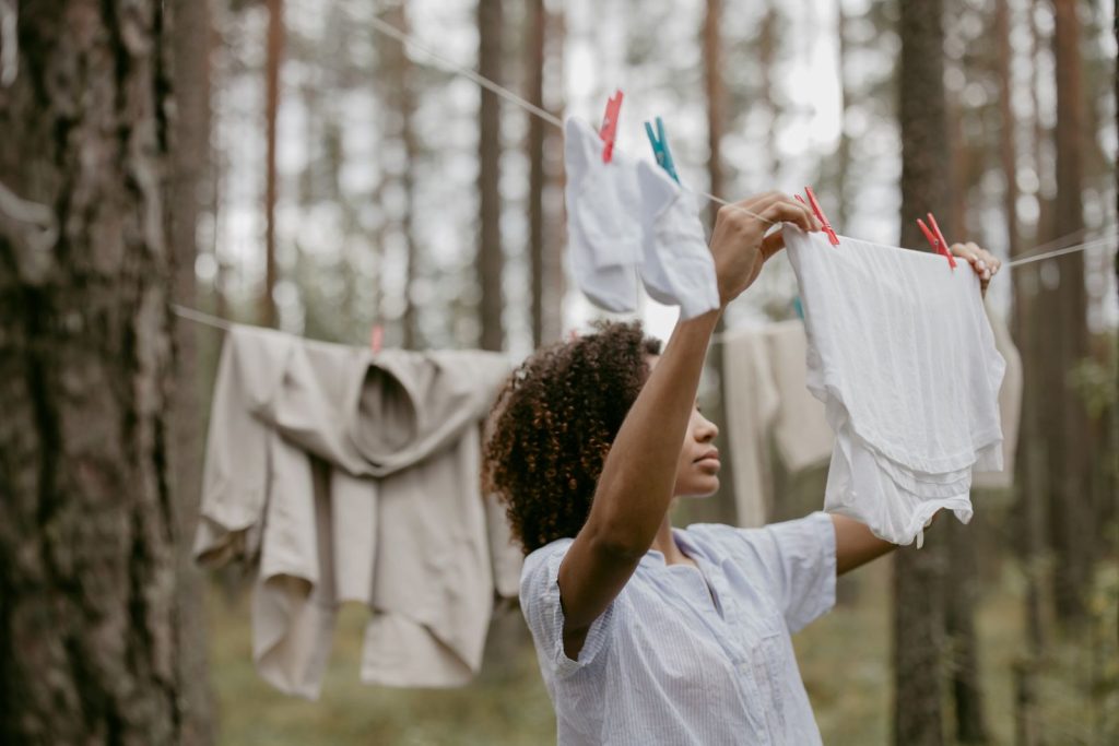An African woman hangs laundry on a clothesline surrounded by a serene forest, blending nature and daily life.