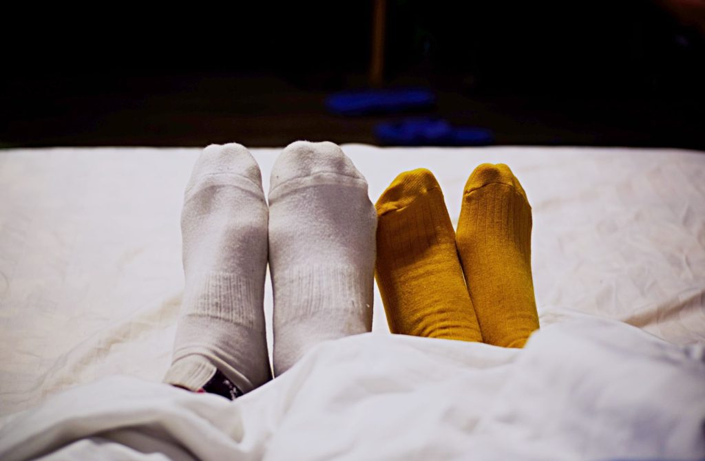 A couple wearing colorful socks relaxes under a duvet, depicting comfort and warmth.