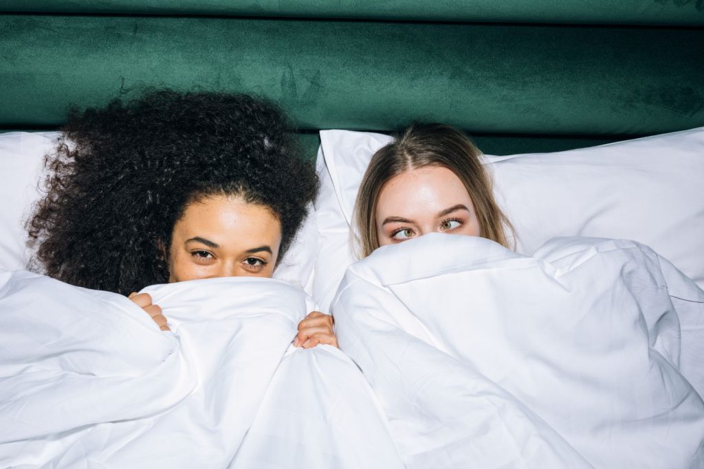 Two young women sharing joyful, cozy moments in bed, embracing happiness and friendship.