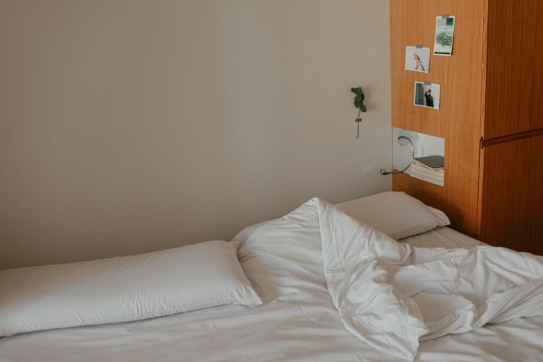 A minimalist bedroom featuring an unmade bed with white sheets and wooden decor.