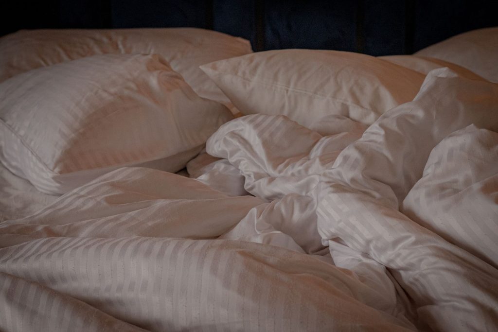 A comfortable and inviting bed with white pillows and a crumpled duvet, perfect for a relaxing setting.