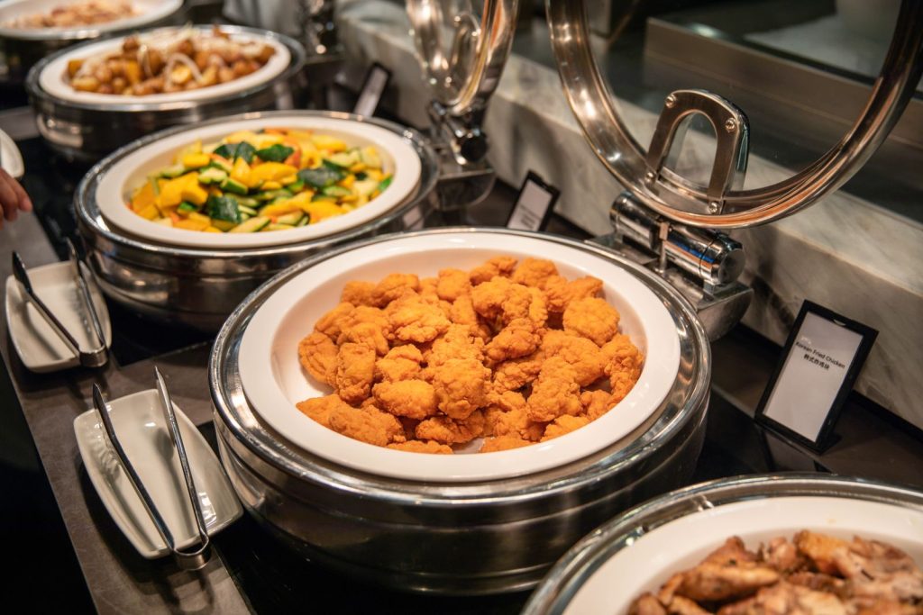 Close-up of a buffet featuring crispy fried chicken and mixed vegetables in chafing dishes.