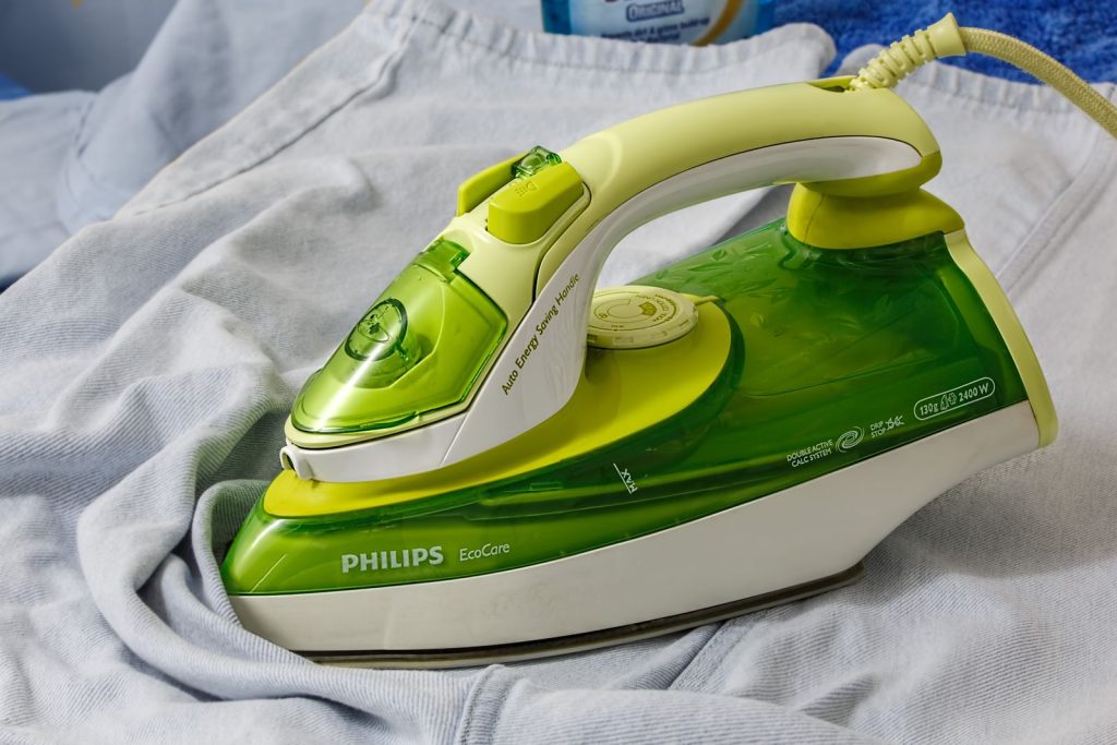Green Philips EcoCare iron on a wrinkled shirt, ready for ironing.