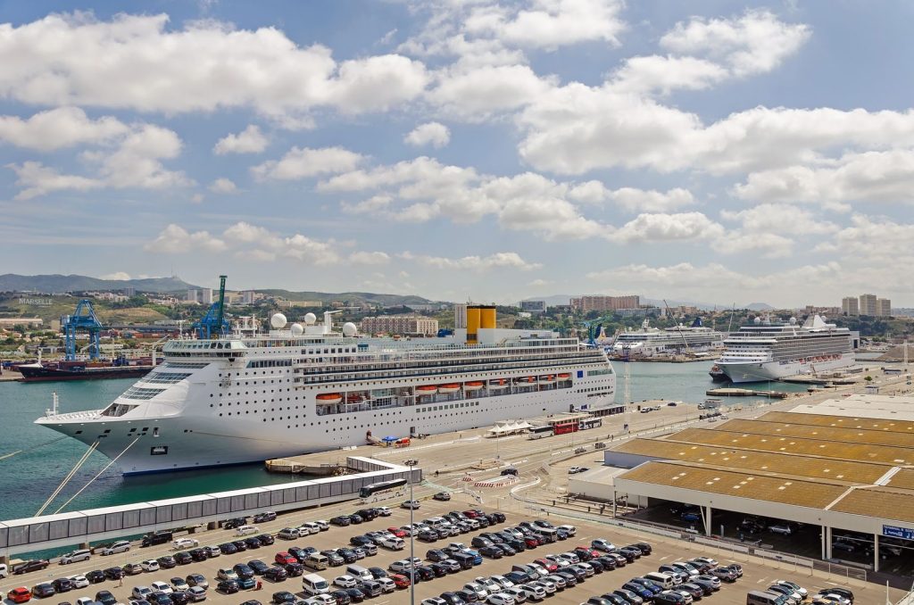 Aerial view of cruise ships docked at a busy port with numerous cars parked nearby.