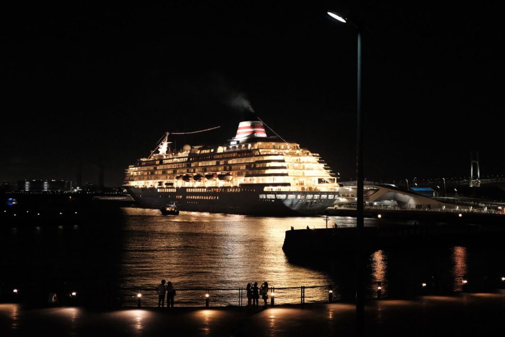 Illuminated cruise ship in night port with city lights, peaceful scene.