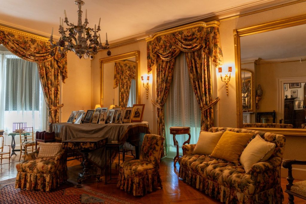 A beautifully decorated vintage living room featuring floral drapes, antique furniture, and a grand chandelier.