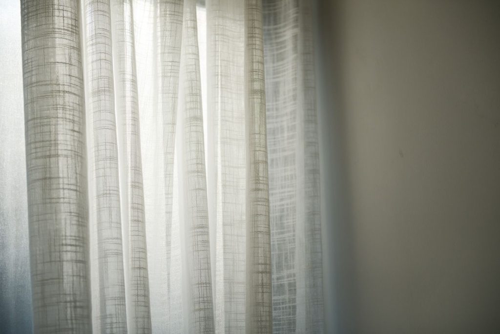 Sheer white curtains gently lit by daylight create subtle shadows on the wall.