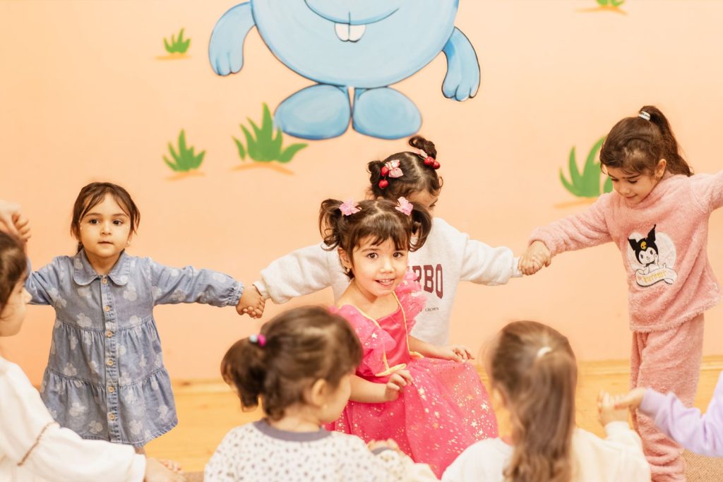 Happy children holding hands in a playful indoor circle game, enjoying a fun activity together.