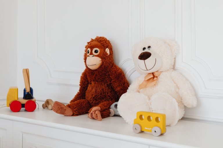 Cute plush teddy and monkey toys with wooden cars on a white shelf, perfect for kids' room decor.