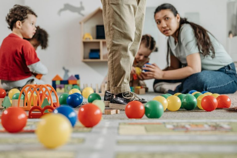 Children and a teacher playing with toys in a kindergarten setting indoors.