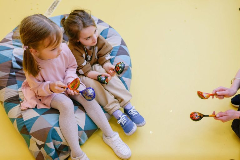 Two children joyfully play maracas indoors, capturing youthful fun on a vibrant beanbag.
