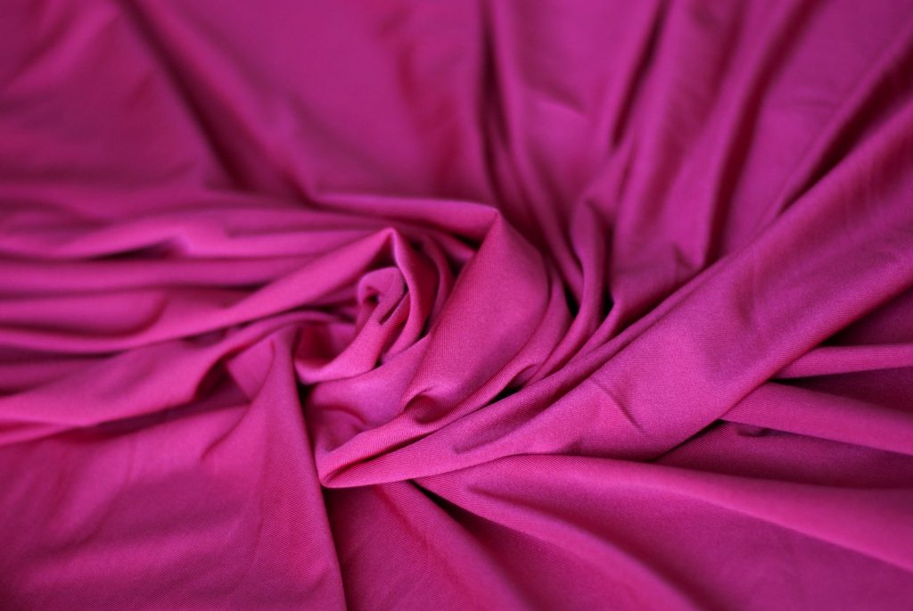 A detailed close-up of vibrant pink fabric with soft wrinkles and a silk-like texture.