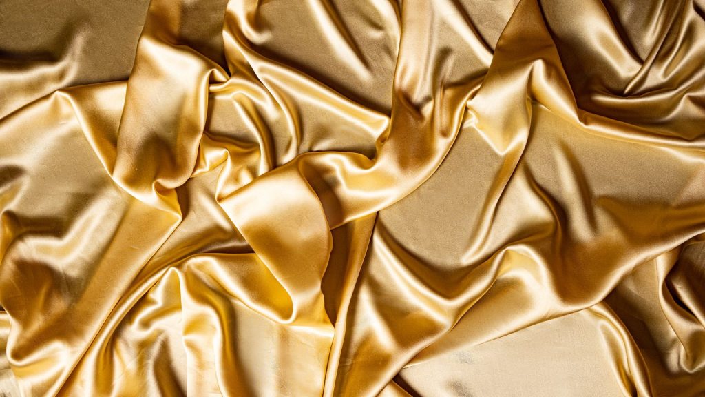 Close-up of golden silk fabric showcasing smooth and crinkled texture.