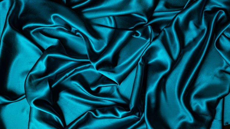 Close-up of crumpled turquoise satin fabric with a smooth and shiny texture, ideal for textile projects.