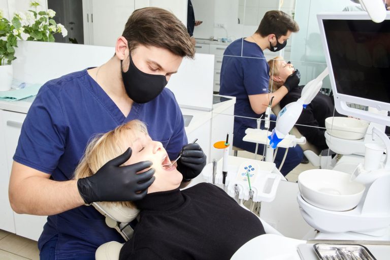 A dentist in a protective mask performing a dental procedure on a patient in a bright clinic.