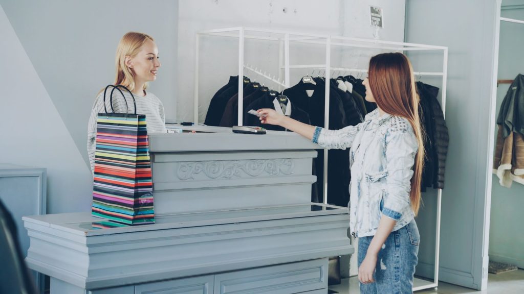 A woman paying by card at a store counter, handing card to female cashier.
