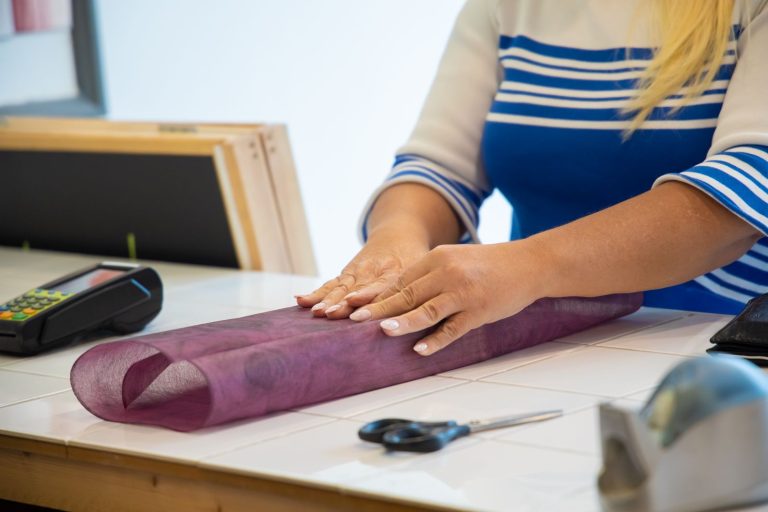 Close-up of a woman wrapping a gift with purple tissue paper indoors. Includes scissors and card reader.
