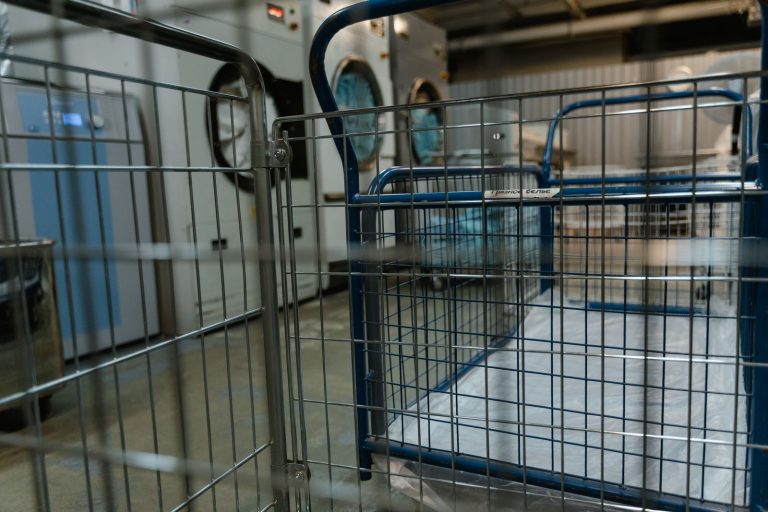 Empty metal baskets and commercial washing machines in a laundry facility.