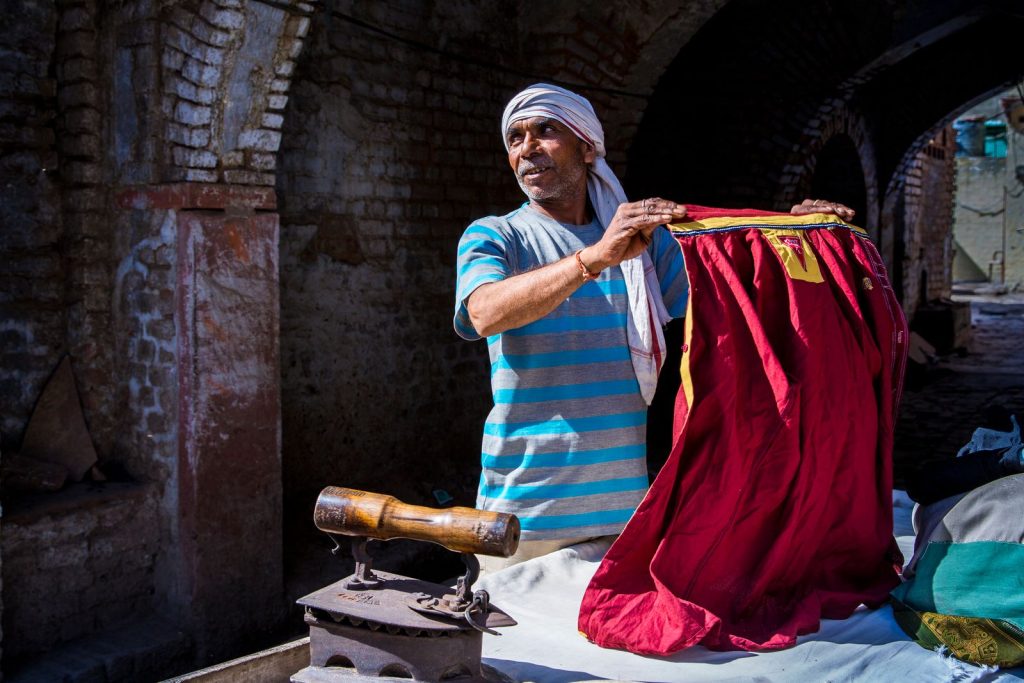 Man ironing clothes on street with vintage iron outdoors, vibrant fabrics.
