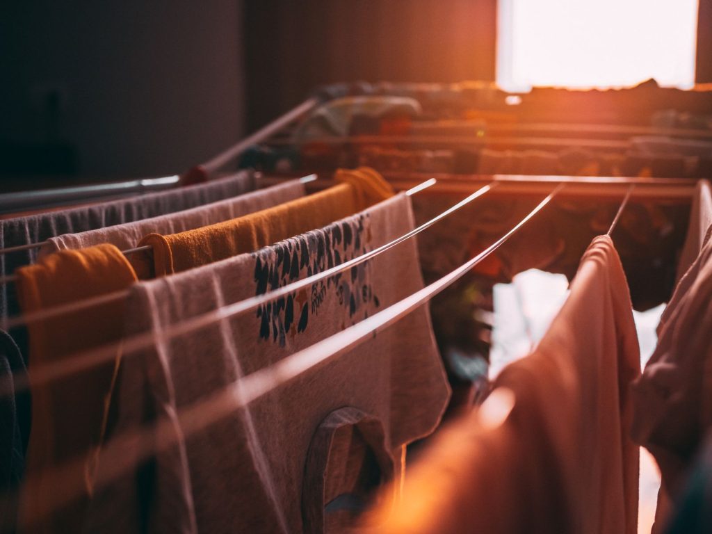 Sunset casts a warm glow on clothes drying indoors on a rack, evoking a cozy ambiance.