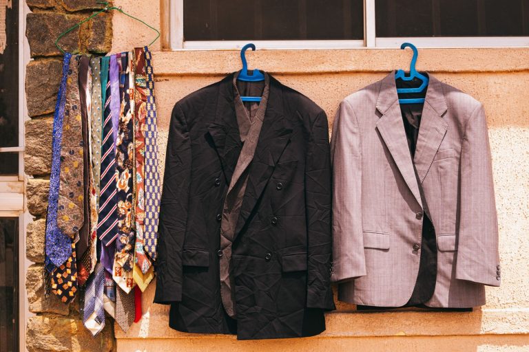 A black and gray suit with colorful ties hanging outdoors on a wall in Jos, Nigeria.