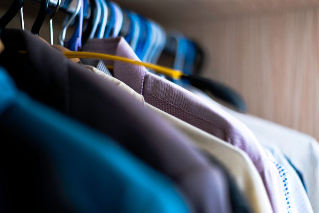 Close-up of various shirts hanging on colorful hangers inside a wardrobe.