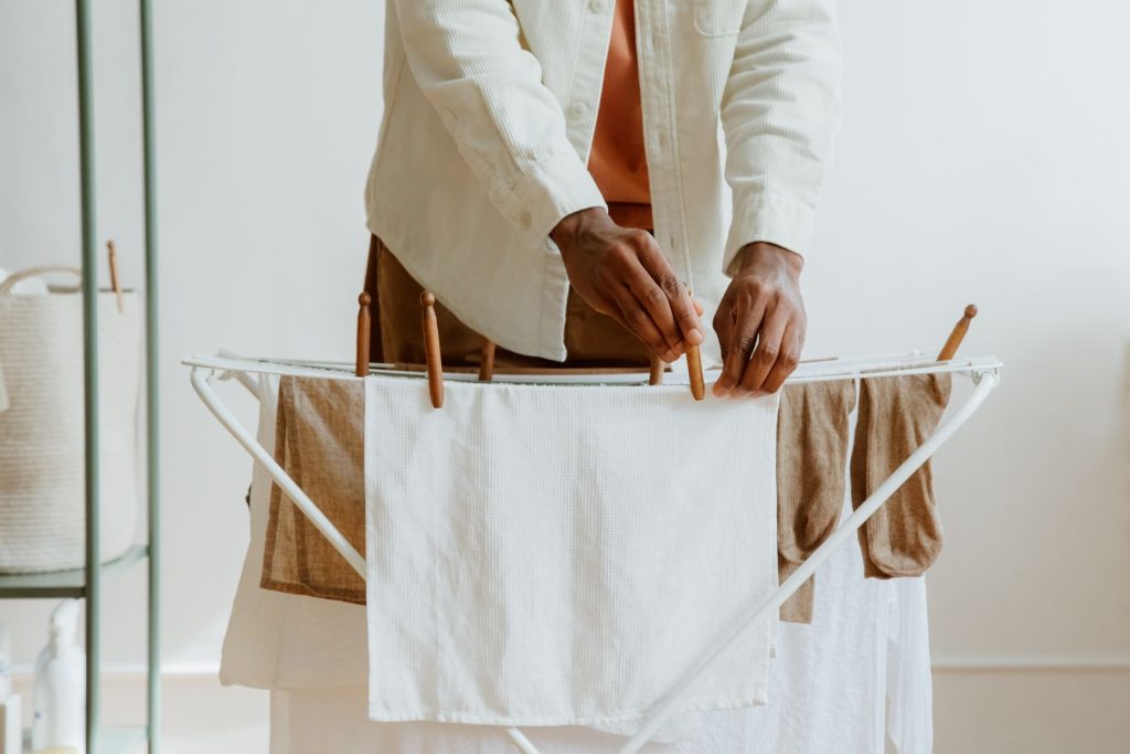 A man uses wooden clips to hang laundry indoors, emphasizing household routines and care.