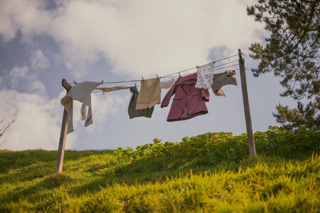Clothes hang on a clothesline in a rural meadow under a summer sky, evoking simplicity and tranquility.