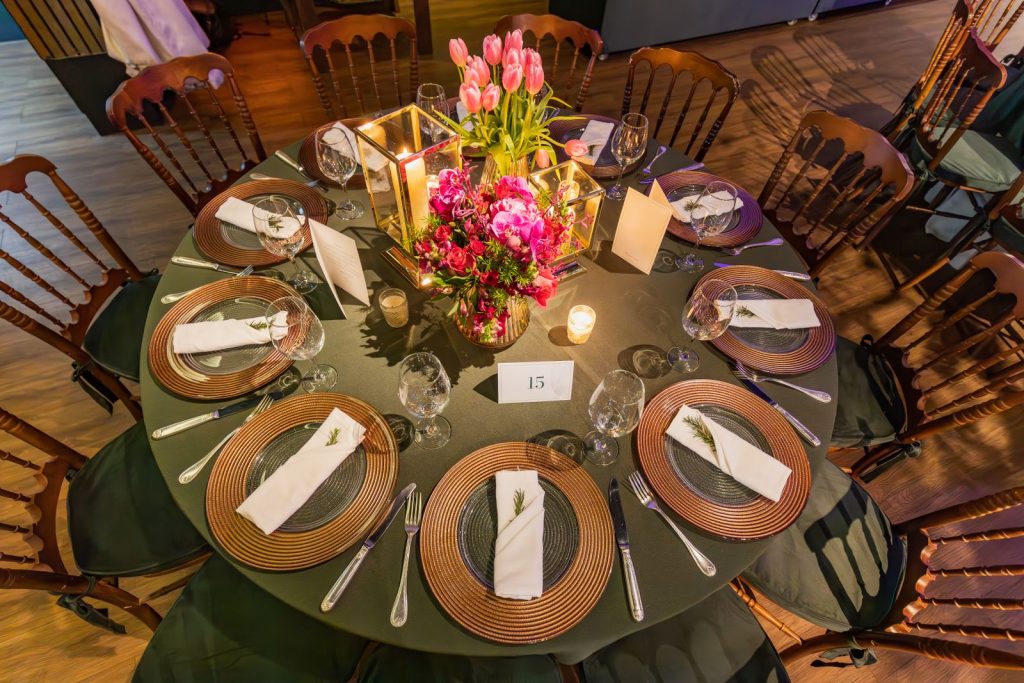 An elegantly decorated round table for a wedding or event, featuring flowers, candles, and fine dining settings.