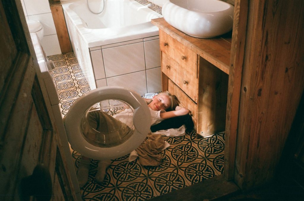 Child lying peacefully on a patterned tiled bathroom floor with a playful smile.