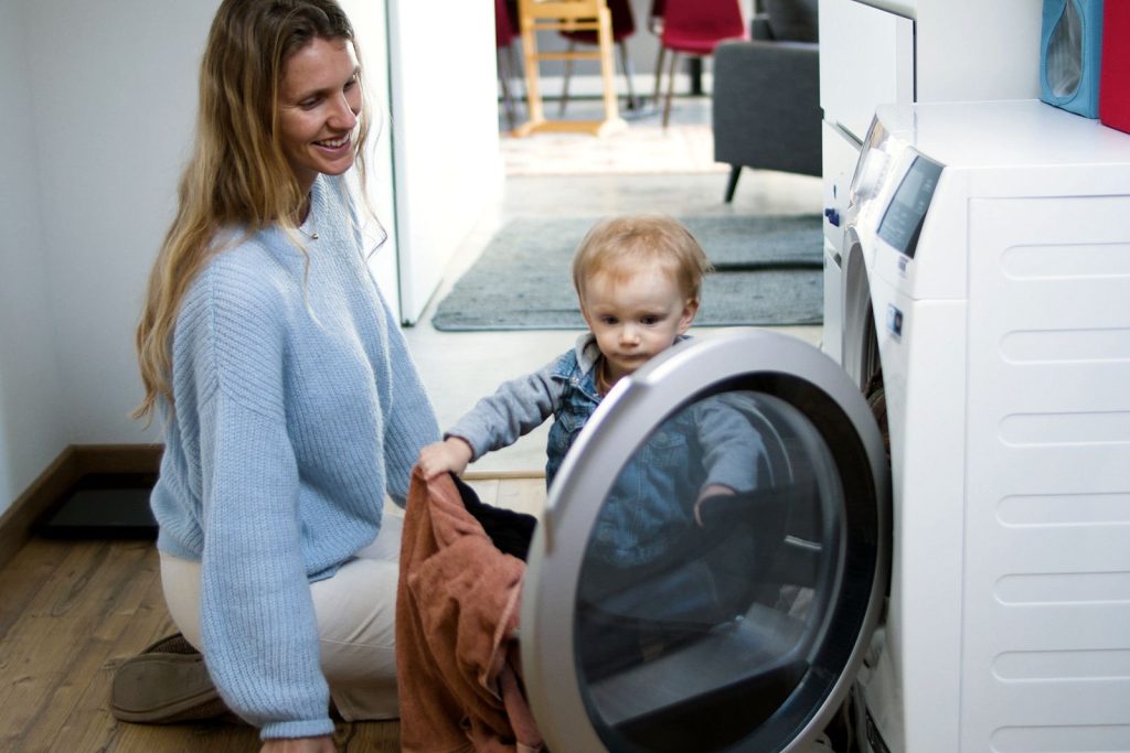 Mother and toddler joyfully doing laundry together, fostering family bonding at home.