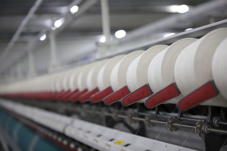 Close-up view of a textile production line showcasing white thread spools in an Indian factory.