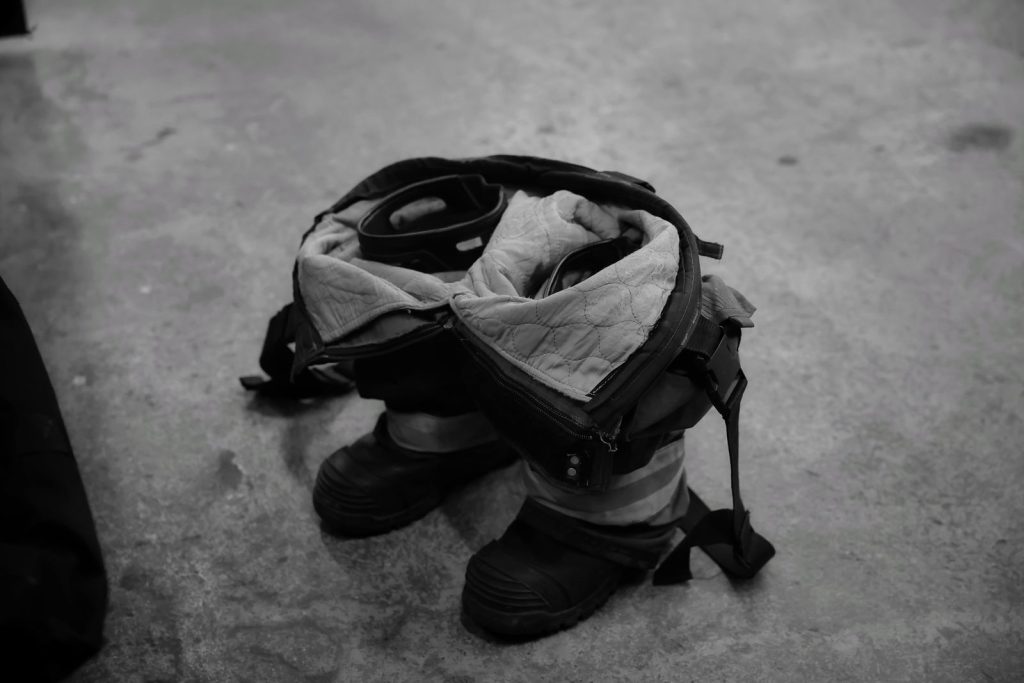 Black and white image showing a firefighter suit laid on a concrete floor, highlighting readiness.