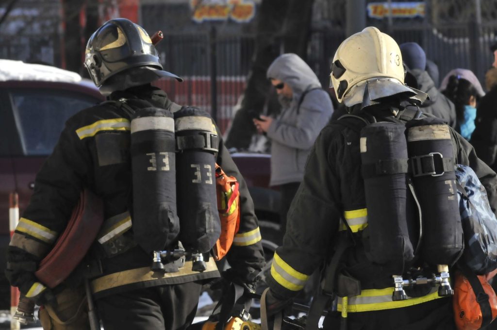 Two firefighters in full gear walking through an urban area.