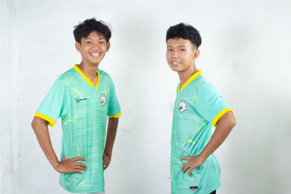 Young football players smiling and posing confidently indoors.