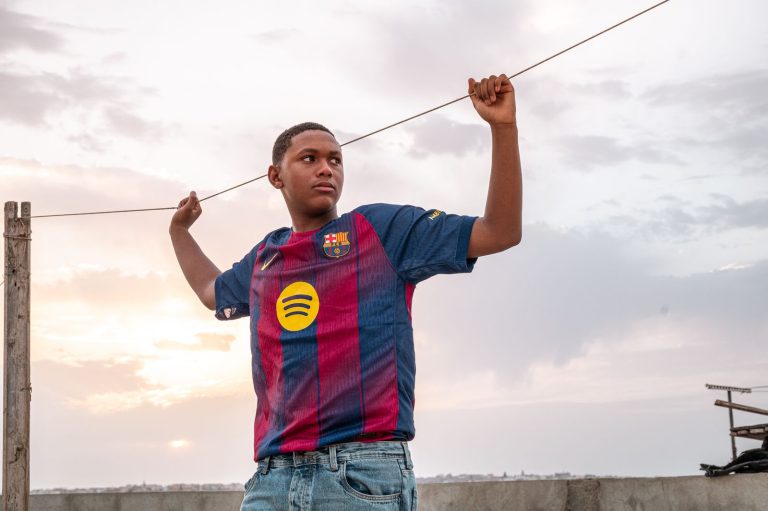 Teenager outdoors in a soccer jersey at sunset, standing confidently.